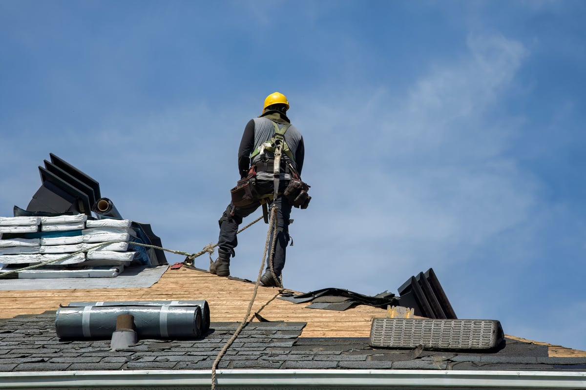 Roofer fixing shingles with a nail gun against a blue sky